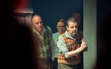 A production shot from The Gorbals Vampire. Two men in knitted vests wait at the side of the stage.