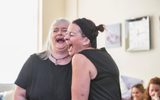 Two women laughing openly. They are both dressed in black and other women can be seen laughing in the background.