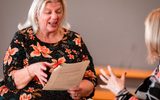 An older woman making an exaggerated facial expression while she reads a script.