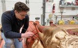 A man painting a statue of an elephant with gold paint.