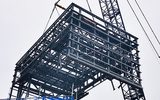 a large crane is pictured lifting a large metal structure into the air. The sky is blue with clouds.