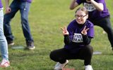 A young person in a purple Citizens Theatre t-shirt crouches on the grass and makes two peace signs with their fingers.