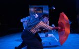 A stage show. A woman is wearing a backpack and holding an open umbrella.