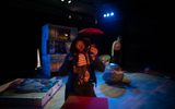 A stage show. A woman is kneeling by a box she is holding a small puppet that looks like her.