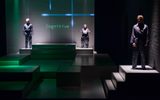 A stage show. Three people in boiler suits stand across the stage. The word 'cognitive' is projected on the wall behind them.