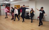 A drama class. A group of young participants and two tutors are pretending to walk a tightrope.