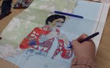 A hand draws a portrait of a woman in coloured felt-tip pens on top of a map.