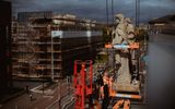 The Citizens Theatre redevelopment building site, two men in high-vis clothing are standing on scaffolding in front of three historic statues on the roof of the theatre. In the background, you can see a main road and construction across the road.