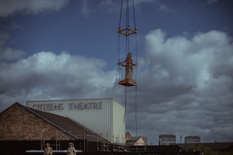 A statue being lowered onto the roof of the Citizens Theatre via a crane.