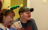 Two women smiling and looking to the left. One is wearing a Christmas Tree headband and drinking a cup of tea.