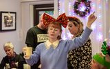 A woman wearing an oversized festive red bow and holding a mug of tea dances with her eyes closed.