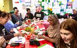 A group of people sit at a table making Christmas crafts.