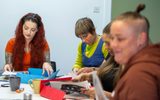 A group of women sit at a table and select magazine pages for a collage activity.