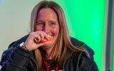 A woman smiles while holding a plastic kazoo to her mouth.