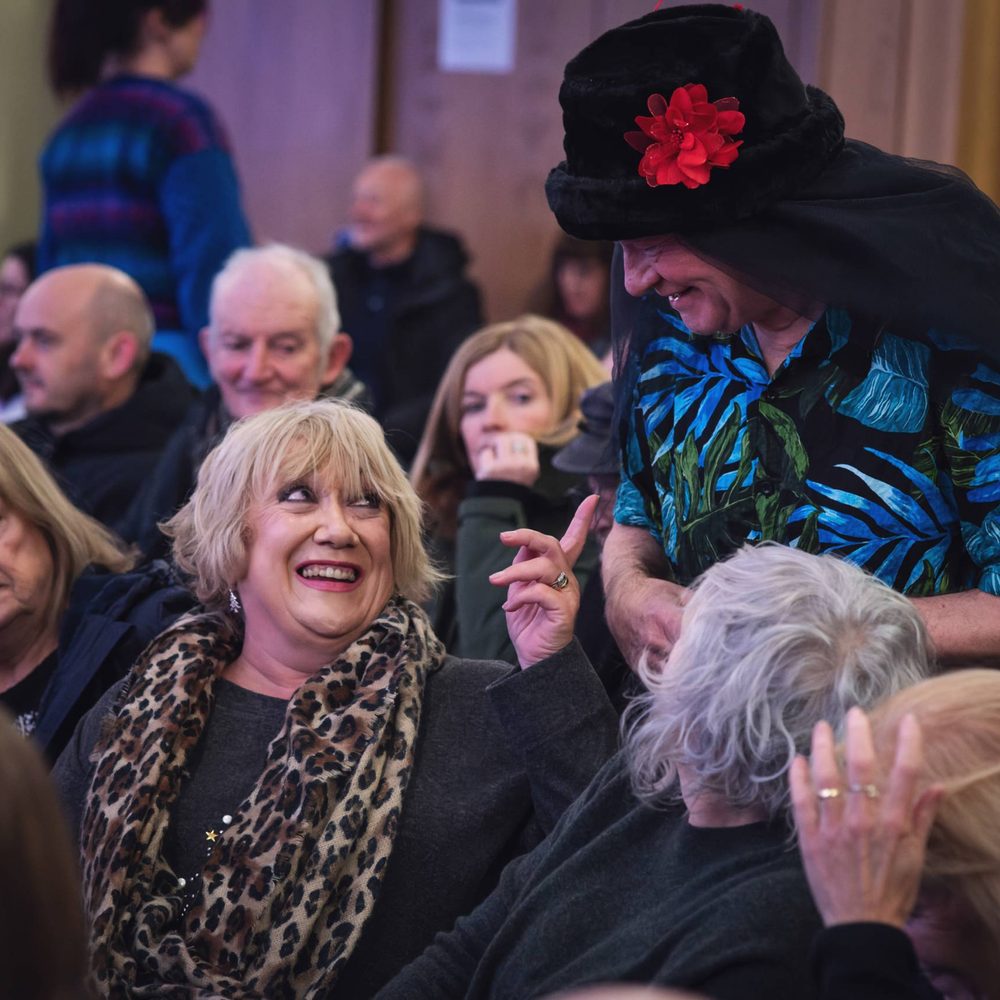 A man walking through a busy audience. An audience member is smiling and pointing at him.