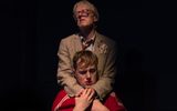 A production shot. An older man stands behind a young one, with his arms around his neck.