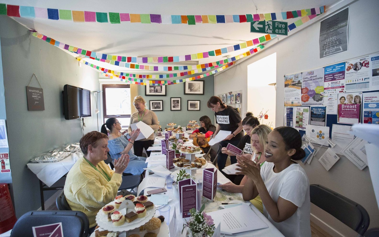 A group of women sitting around a long trestle table. The room is decorated with colourful bunting.