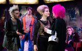 A highly theatrical production image of a show. Everybody is wearing punk style clothing. They are on a stage with graffiti style surroundings.