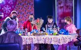 A highly theatrical production Image of a theatre show. A group of actors in old, dishevelled, Victorian style clothing are sitting round a large dining table.