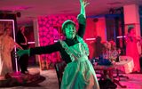 A highly theatrical production Image of a theatre show. A woman in a dishevelled maids costume is standing with her hands in the air.