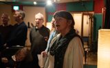 A group of people singing in a recording studio. One woman is in focus at the centre of the frame.
