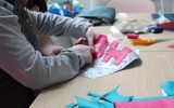 A faceless figure pins fabric letters to a piece of fabric in preparation for sewing.