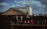 A statue being lowered onto the roof of the Citizens Theatre. Two have already been placed. The theatre's name appears in large lettering behind the statues.