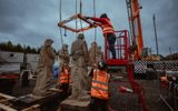 The statues preparing to be lifted onto the roof. People in hi-viz vests are securing the crane onto one of the statues.