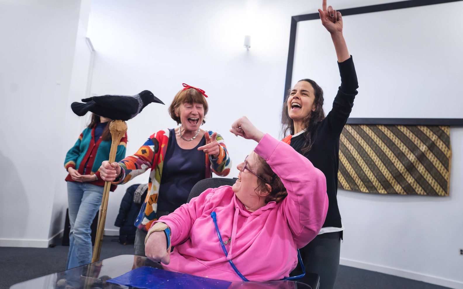Four women rehearsing for a show. They are smiling and pointing their fingers in the air.