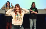 Three young people dancing on the stage/ A screen behind them says ' I love this musical! I know all the words and all the moves.'