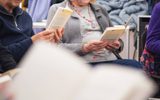 A play reading session. A woman in glasses reads from a book.