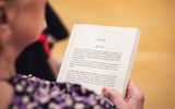 A play reading session. A woman holds a book open, with the first page in focus.
