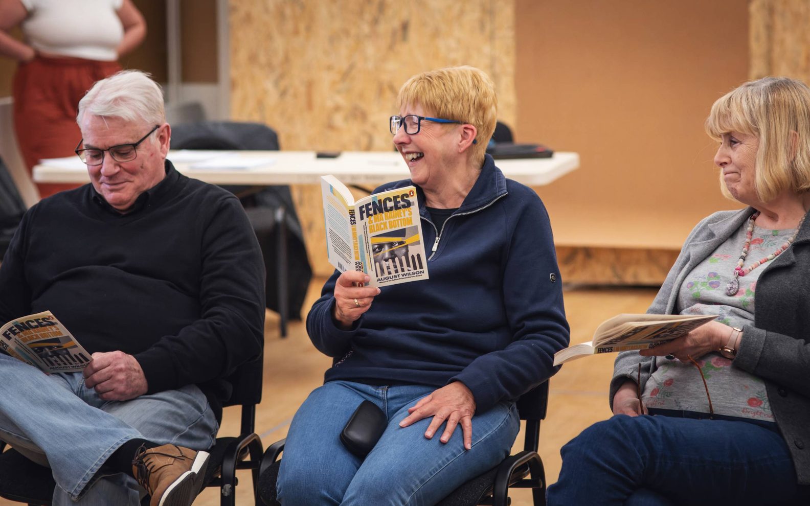 A play reading session. Two women and a man sitting in a row and holding copies of the play 