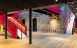 Inside the newly refurbished Citizens Theatre foyer. A bright pink, modern staircase runs alongside the older exposed brick wall.
