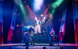 Cast dancing on stage, there are colourful lights