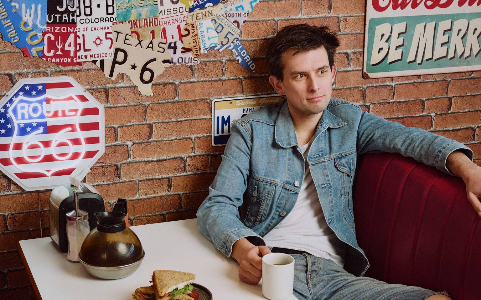 A man sitting at a dinner table, he's wearing all denim. It has an American feel.