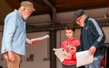 Two men with a young boy in between the. They are holding scripts and dressed casually.