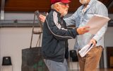 Two men are dressed casually. They are holding scripts. They are walking towards each other about to start dancing.