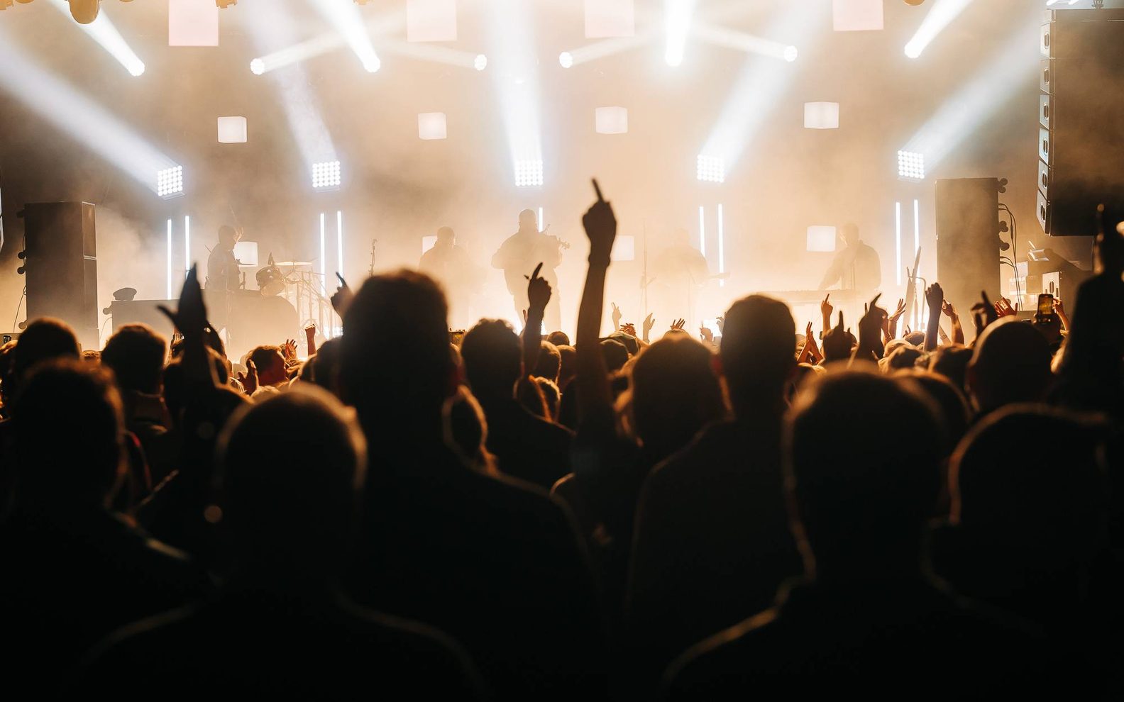 A crowed witharms in the air looking up at a bright stage