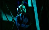 A female actor wearing a blue boiler suit is lurking in the shadows.