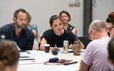 Actors reading scrops around a table.