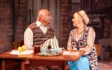 Samantha Power and Bhasker Patel as George and Ella in East is East. They are sat at a 1970s style kitchen sharing a cup of tea.