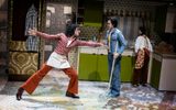 Two young men play fighting in a 1970s style kitchen. A younger girl is standing at the kitchen sink.