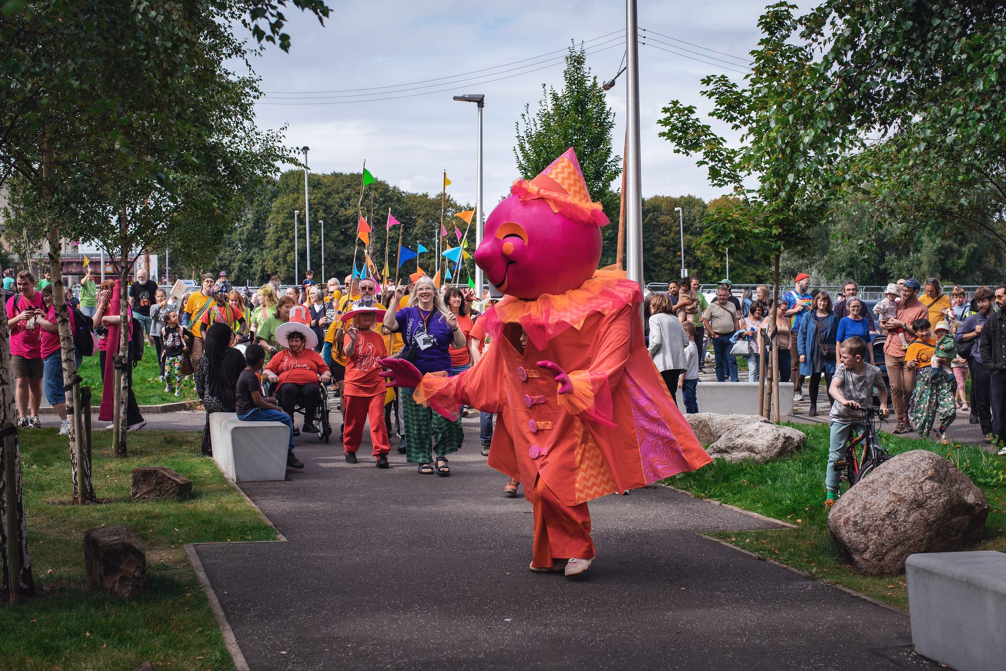 A large pink and orange puppet leading a procession down a street in Glasgow.