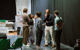 A group of about five people, of different genders and ethnicities, standing and chatting together in a rehearsal room.