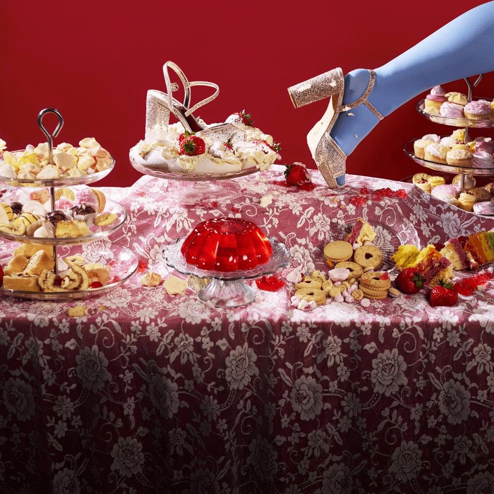 A colourful table covered in cakes. Cindella's sparkly shoe is left in a pavlova.