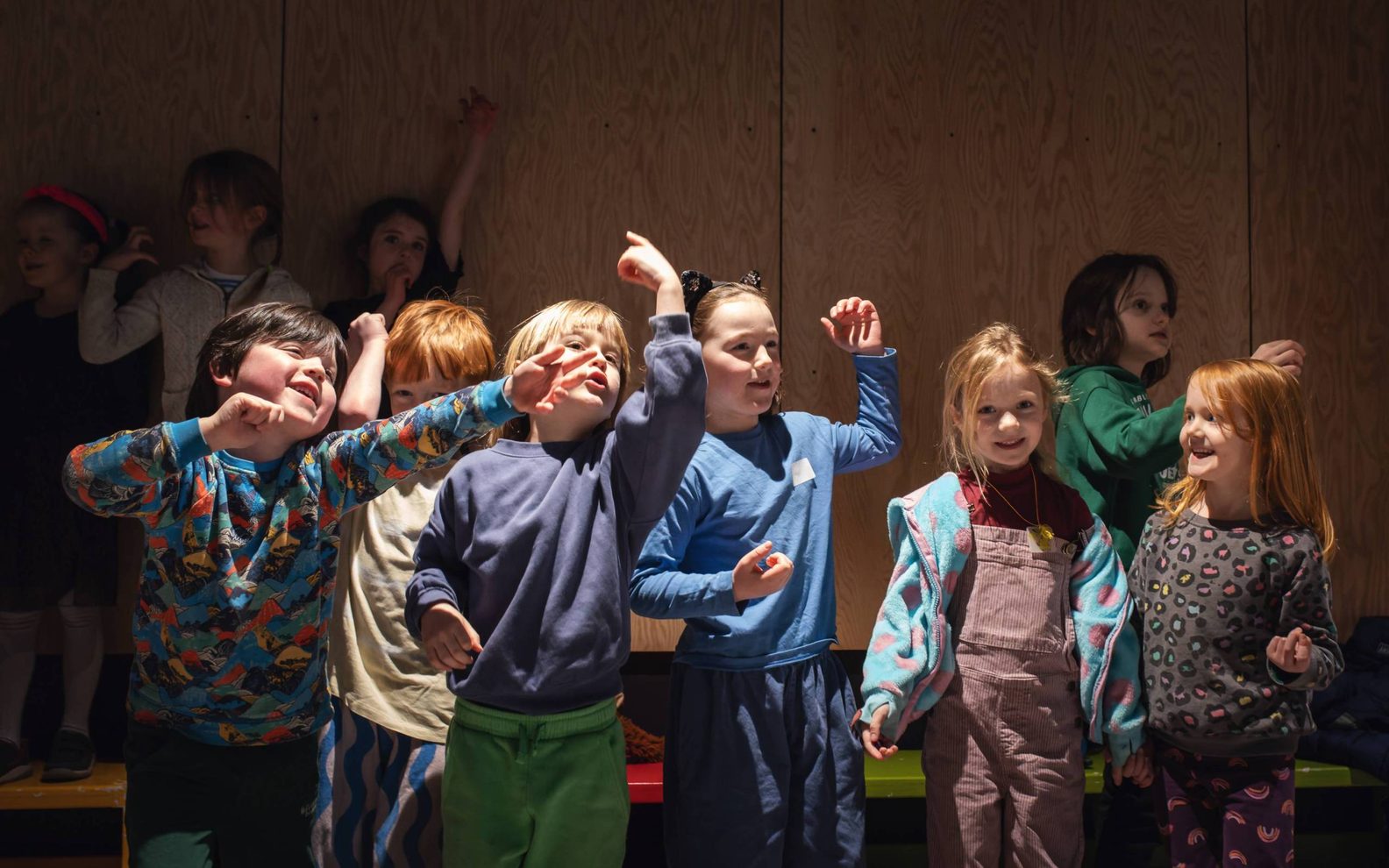 A group of children in colourful clothes, smiling with their left arms raised.