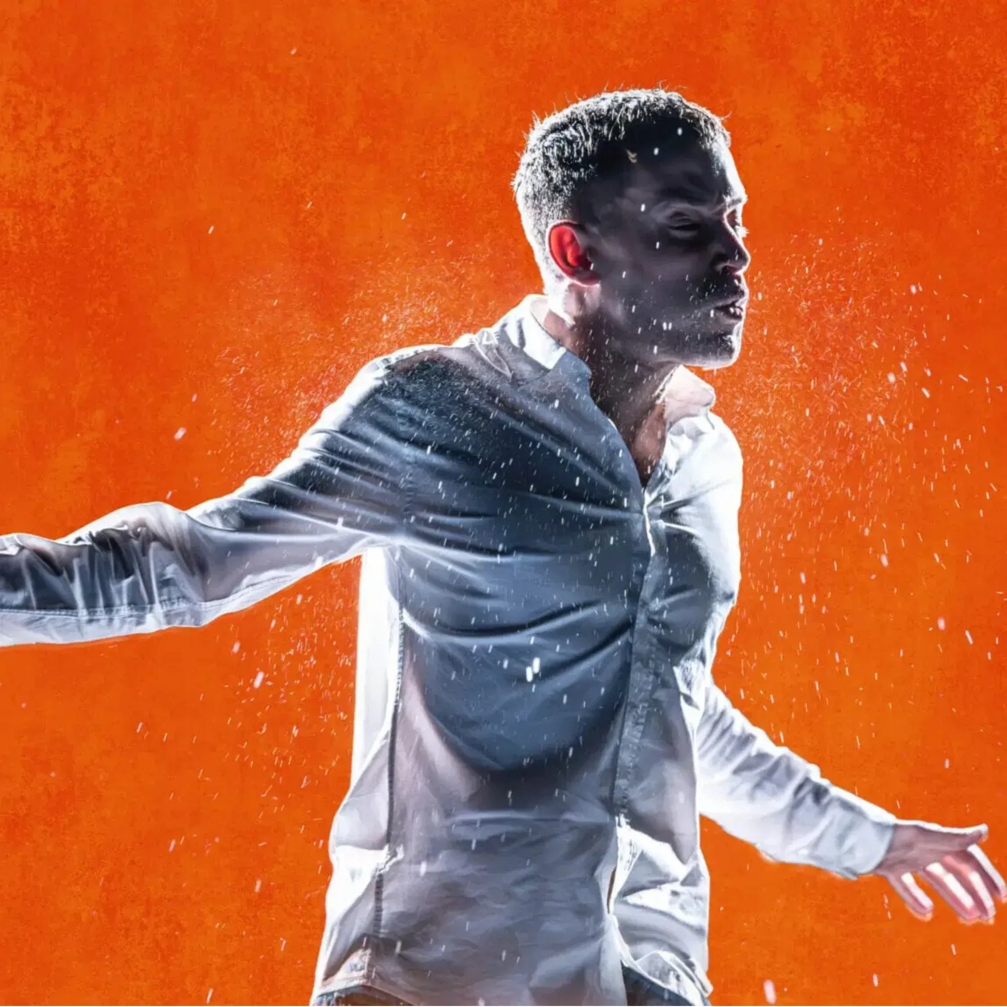 A man is standing with his arms outstretched. He isstaring into the distance. The background is orange.